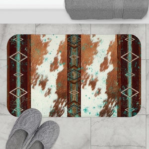 Puede incluir: Una alfombra de baño de piel de vaca marrón y blanca con diseños geométricos turquesa y marrón en los lados.