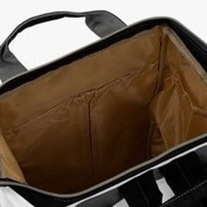 May include: The inside of a black and white striped diaper bag with a brown lining. The bag has a zipper closure and a large main compartment. There are several pockets on the inside of the bag, including a zippered pocket and a mesh pocket.