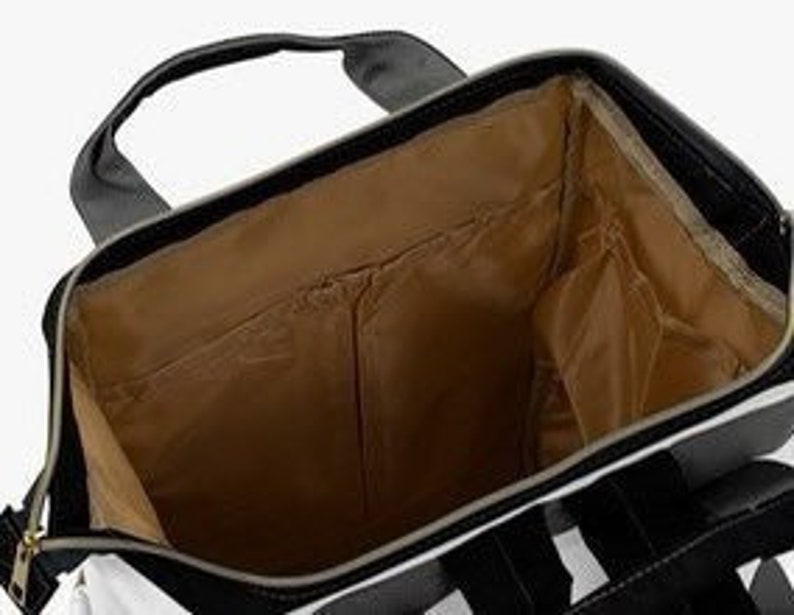May include: The inside of a black and white striped diaper bag with a brown lining. The bag has a zipper closure and a large main compartment. There are several pockets on the inside of the bag, including a zippered pocket and a mesh pocket.