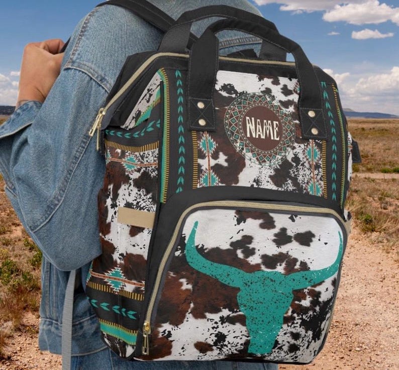 Personalized brown and white faux cowhide print with southwestern tribal design, western style diaper bag backpack. Custom monogrammed with your name or initials. Faux animal print backpack with a turquoise longhorn bull skull