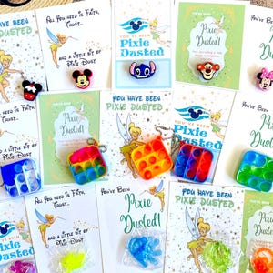 May include: A collection of rectangular cards featuring Tinker Bell illustrations and the text You Have Been Pixie Dusted, accompanied by various colorful silicone character charms and small square bubble-popping fidget toys in plastic packaging.
