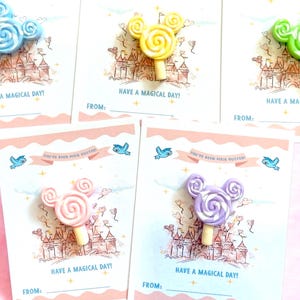 May include: Five greeting cards with Mickey Mouse-shaped lollipops in blue, yellow, green, pink, and purple. Each card has a castle illustration and the text "HAVE A MAGICAL DAY!" and "FROM:" at the bottom. The cards are on a pink background.