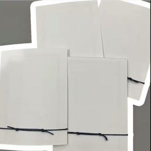 Peut inclure: Plusieurs cartes rectangulaires blanches, attach&eacute;es avec de la ficelle noire. Les cartes sont dispos&eacute;es en composition superpos&eacute;e, certaines chevauchant les autres. La ficelle est nou&eacute;e simplement, fixant les cartes. Le fond est gris neutre.