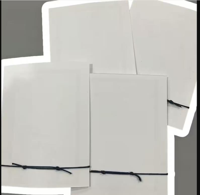 Peut inclure: Plusieurs cartes rectangulaires blanches, attach&eacute;es avec de la ficelle noire. Les cartes sont dispos&eacute;es en composition superpos&eacute;e, certaines chevauchant les autres. La ficelle est nou&eacute;e simplement, fixant les cartes. Le fond est gris neutre.