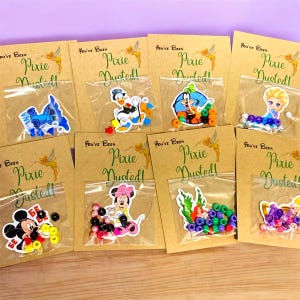 May include: Assortment of small plastic bags with character stickers and colorful beads. Each bag is attached to a brown card with the text "You've Been Pixie Dusted!". Characters include Mickey Mouse, Minnie Mouse, and Elsa.