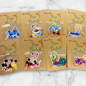 May include: Assortment of small clear bags containing colorful beads and character stickers, including Mickey Mouse, Minnie Mouse, and Elsa. Each bag is attached to a brown card with the text "You've Been Pixie Dusted!"
