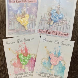 May include: Four greeting cards with colorful illustrations and lollipop accents. Two cards say "You've Been Pixie Dusted!" and feature a castle. The other two say "You're So Sweet" with the text "Thanks for making my day more magical!"