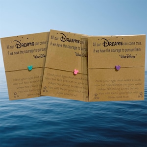 Peut inclure: Trois bracelets de v&oelig;ux sur le th&egrave;me de Disney. Chaque bracelet pr&eacute;sente un petit charme en forme de t&ecirc;te de Mickey Mouse en bleu sarcelle, rose et violet. Les cartes indiquent "Tous nos r&ecirc;ves peuvent se r&eacute;aliser si nous avons le courage de les poursuivre."