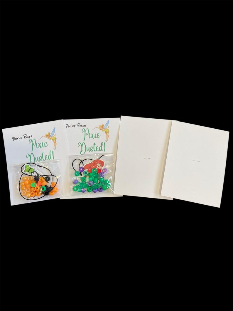 May include: Two cards with the text "You've Been Pixie Dusted!" and a Tinkerbell graphic. Two small bags of colorful beads are attached to the cards. Two blank cards are also included.