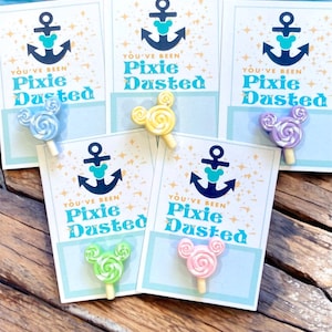 May include: A collection of cards with the text "YOU'VE BEEN Pixie Dusted" and an anchor design. Each card holds a colorful, Mickey Mouse-shaped lollipop. The lollipops are in various colors, including blue, yellow, green, pink, and purple.