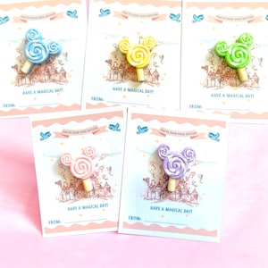 May include: Five greeting cards with Mickey Mouse-shaped lollipops in blue, yellow, green, pink, and purple. Each card has the text "HAVE A MAGICAL DAY!" and "FROM:" with a castle illustration and a pink border.