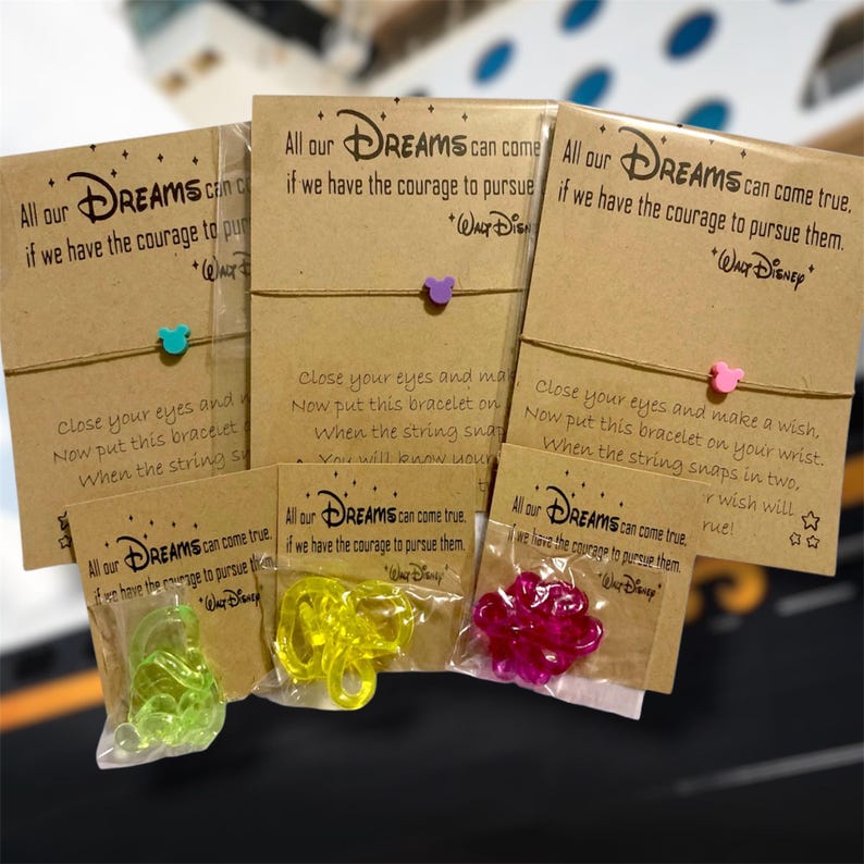 Peut inclure: Plusieurs bracelets de v&oelig;ux sur le th&egrave;me de Disney. Chaque bracelet est orn&eacute; d'un petit charme de couleur bleue, violette et rose. Les cartes indiquent : "Tous nos r&ecirc;ves peuvent se r&eacute;aliser si nous avons le courage de les poursuivre."