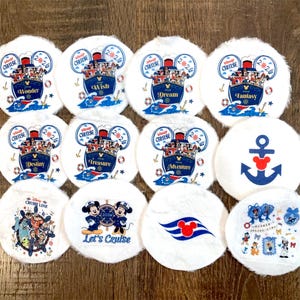May include: A collection of white, round, plush items with various Disney Cruise Line designs. Designs include cruise ships, Mickey Mouse, anchors, and the text "Cruise 2026", "Let's Cruise", and ship names like "Wonder" and "Dream".