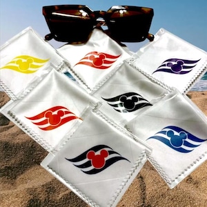 May include: Tortoiseshell sunglasses rest above a collection of white microfiber cleaning cloths. Each cloth features a different color Mickey Mouse head and wave design, including yellow, red, black, purple, and blue.