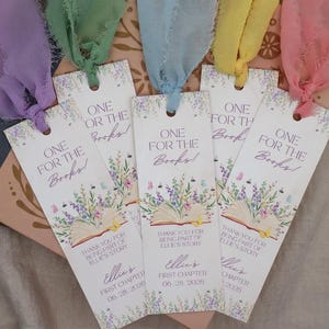 May include: Five rectangular paper bookmarks with colorful silk ribbons in purple, green, blue, yellow, and pink. Each bookmark features a floral illustration, an open book, and the text One for the Books, Thank you for being part of Ellie's story.