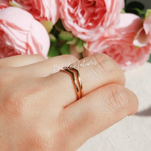 Könnte beinhalten: Ein goldener Chevron-Ring mit zwei Bändern. Der Ring befindet sich an einem Finger.