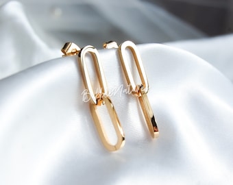 May include: Gold-colored link earrings. Each earring features two elongated, oval-shaped links connected to a post. The earrings are displayed on a white, satin-like fabric. The earrings have a polished, reflective surface.