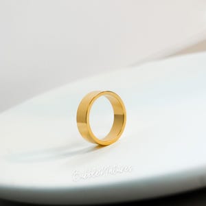 May include: A gold ring with a flat, rectangular band. The ring is set against a white background, with the words "BubbleNatures" in cursive script at the bottom. The ring is a simple, elegant design.