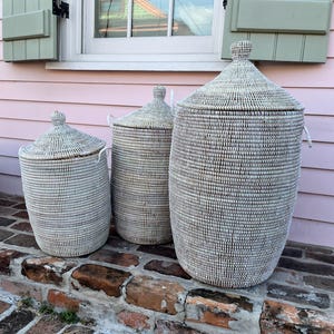 May include: Three white woven storage baskets with lids, arranged in size order from smallest to largest, on a brick step.