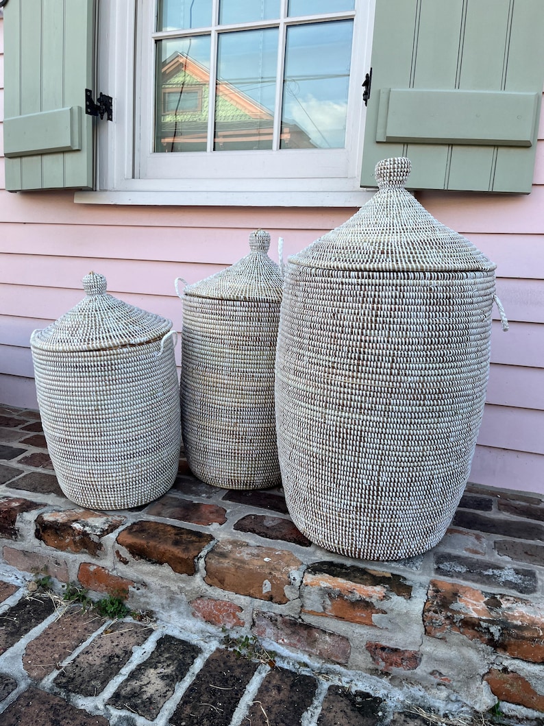 May include: Three white woven storage baskets with lids, arranged in size order from smallest to largest, on a brick step.