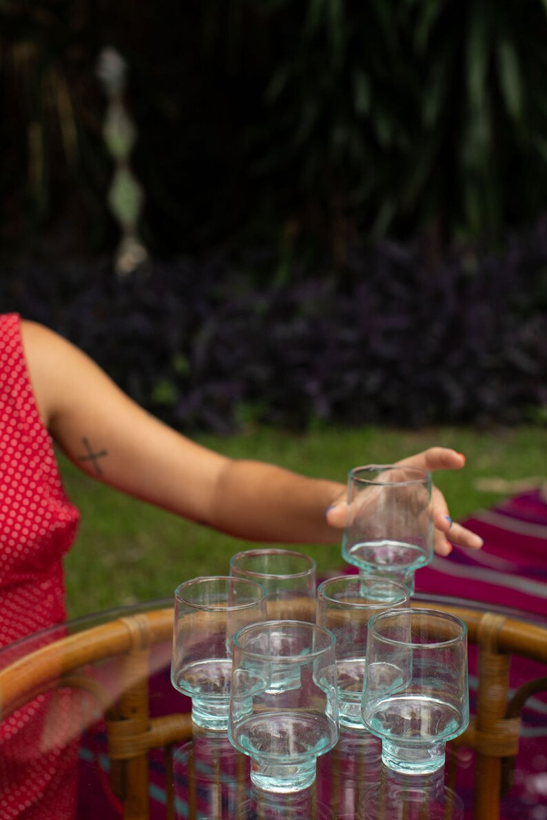 May include: A set of six clear glass tumblers with a textured surface. The glasses are arranged on a round, wooden table with a glass top.