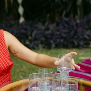 May include: A set of six clear glass tumblers with a unique, textured design. The glasses are arranged on a table with a woven pattern.