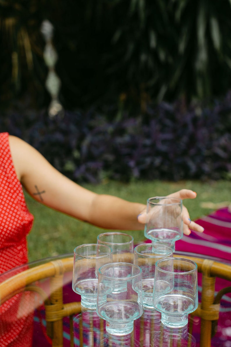 May include: A set of six clear glass tumblers with a unique, textured design. The glasses are arranged on a table with a woven pattern.