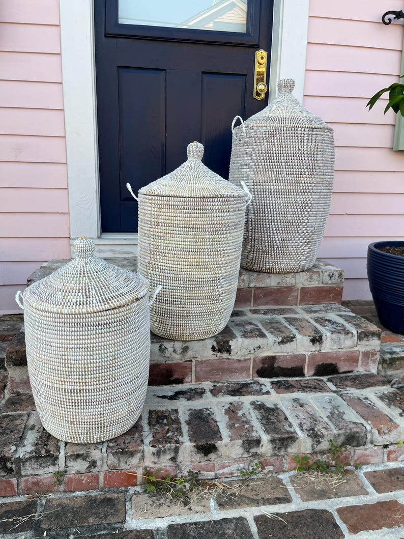 May include: Three white woven storage baskets with lids, arranged on a brick staircase. The baskets are of different sizes, with the largest at the top and the smallest at the bottom.