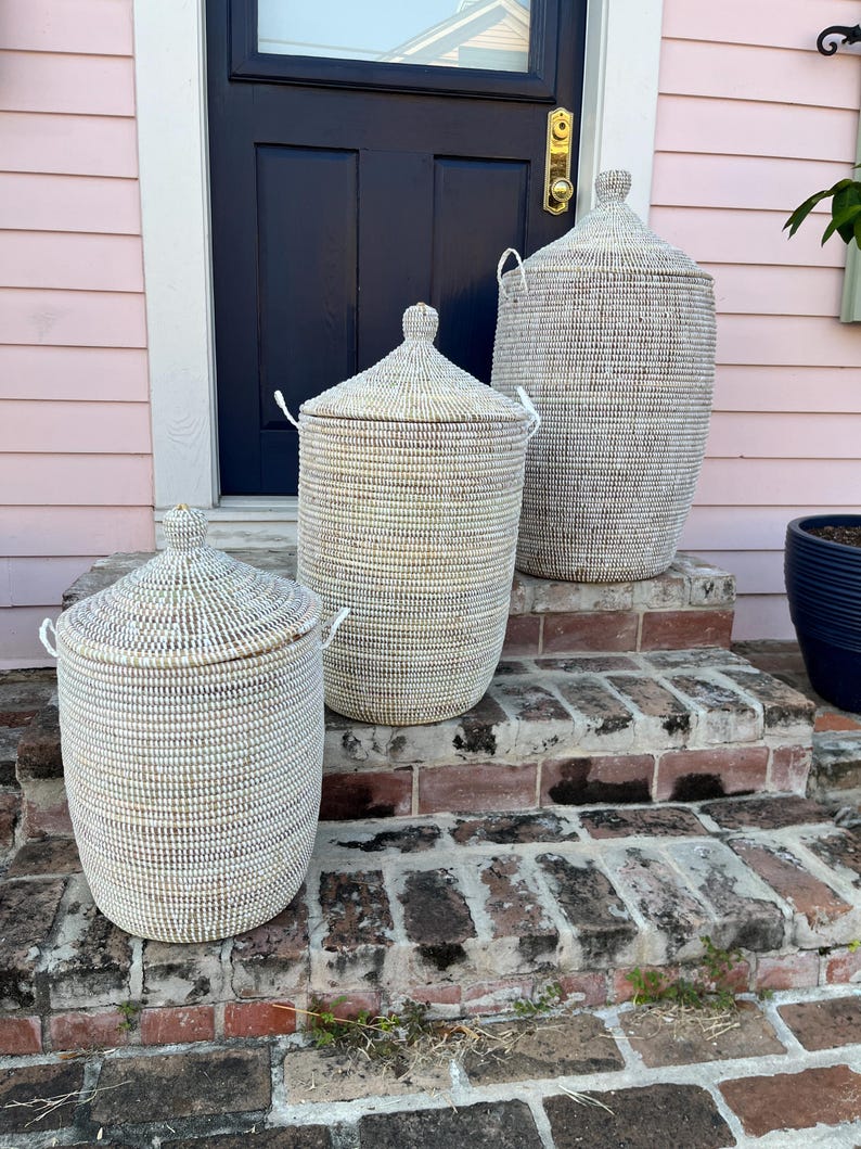 May include: Three white woven storage baskets with lids, arranged in size order on a brick staircase. The largest basket is on the top step, the medium basket is on the middle step, and the smallest basket is on the bottom step.