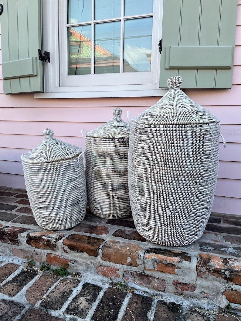 May include: Three white woven storage baskets with lids, arranged in size order on a brick step. The baskets are made of natural materials and have a subtle pattern.