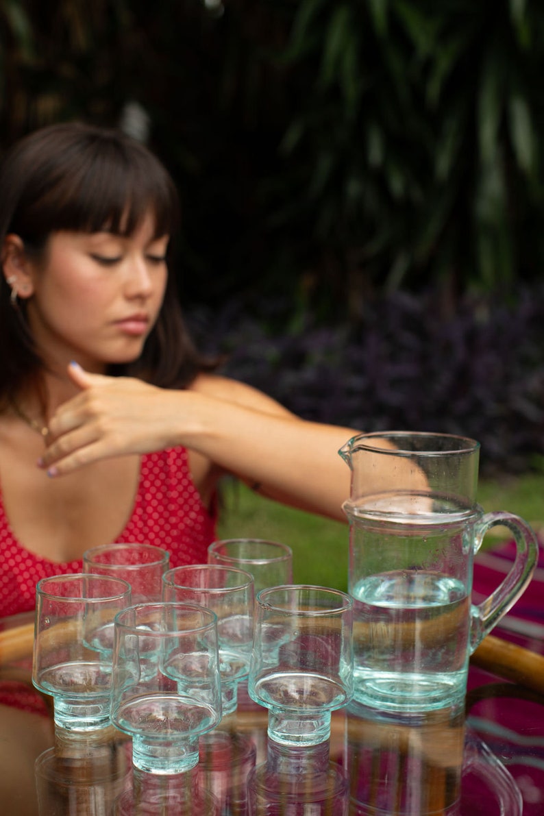 May include: A set of eight clear glass tumblers with a textured base, arranged on a table with a pitcher of water. The tumblers are stacked in two rows of four, with the pitcher in the center.