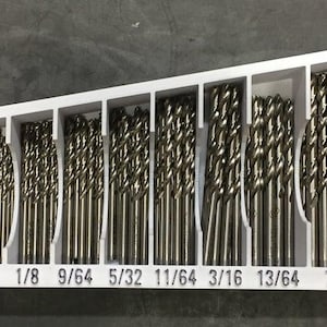 May include: A white plastic drill bit organizer with 18 slots. The slots are labeled with the following drill bit sizes: 1/16, 5/64, 3/32, 7/64, 1/8, 9/64, 5/32, 11/64, 3/16, 13/64, 7/32, 15/64, and 1/4.