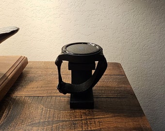 May include: A black smartwatch with a black band is displayed on a black stand. The stand is on a wooden surface.