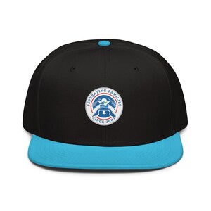 May include: Black flat-brim baseball cap with a light blue brim and top button. The cap features a circular patch with the text "Separating Families Since 2003" around a graphic of a bird and a guitar.
