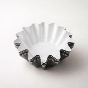 May include: A stack of white, scalloped-edge bowls. The bowls have a glossy finish and a flower-like shape. The bowls are stacked on top of each other, with the edges of the bowls visible. The bowls are a neutral color and would be suitable for serving food.