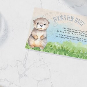 Puede incluir: Una tarjeta azul claro con una ilustración de acuarela de una nutria bebé. La tarjeta dice "Libros para bebé" e incluye un mensaje pidiendo a los invitados que traigan un libro en lugar de una tarjeta para ayudar a que la biblioteca del bebé crezca.