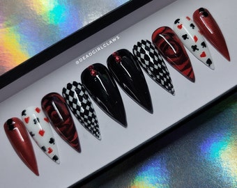 May include: Set of ten false nails with a red, black, and white checkered design, a red rose design, and a playing card design. The nails are in a white box with the text "@deadgirlclaws" on the box.