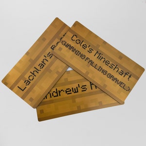 Pu&ograve; includere: Tre targhe in legno a tema Minecraft con i nomi. La targa superiore recita "Cole's Mineshaft WARNING FALLING GRAVEL". La targa centrale recita "Andrew's" e la targa inferiore recita "Lachlan's".