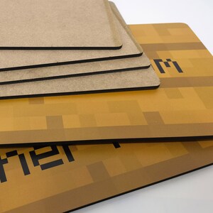 Pu&ograve; includere: Un set di quattro sottobicchieri marroni con bordi neri. I sottobicchieri presentano un design a pixel di un blocco Minecraft dorato.