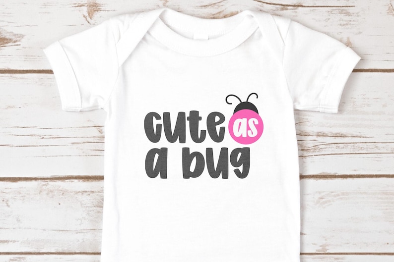 White baby onesie printed with ‘cute as a bug’ using Jelly Puff, a cute chunky handwritten font. Dark gray letters with a pink ladybug ‘as’ circle and tiny antenna. Playful all-caps mix-case style for baby shirts, heat-transfer vinyl, and Cricut/Silhouette projects.
