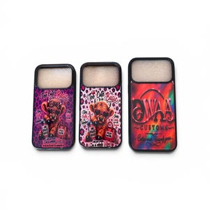 May include: Three phone cases with black borders. Two cases feature a cartoon Highland cow wearing sunglasses and holding a purse, with the text "Too Cute to be Basic". The third case has a red and orange gradient with "WAA CUSTOMS" text.