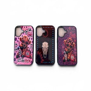 May include: Three phone cases with unique designs. One case features a pink leopard print with a cartoon cow wearing sunglasses and holding a drink and a shopping bag. The second case has a skull and sunflower design. The third case has a purple leopard print with a cartoon cow.