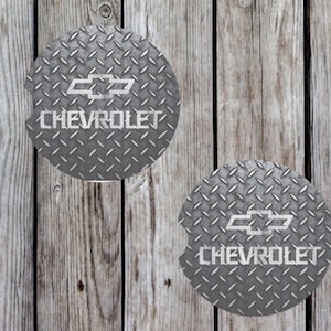May include: Two round gray and silver car coasters with a diamond plate pattern. The coasters feature a silver Chevrolet logo and the word "CHEVROLET" in white.