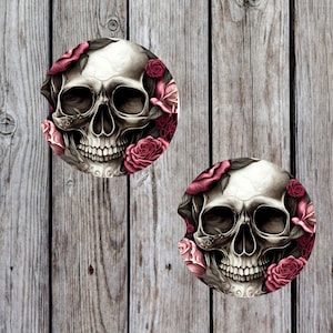 May include: Two round coasters with a skull and pink roses design. The skull is white with black eye sockets and a black mouth. The roses are a dark pink with white centers.