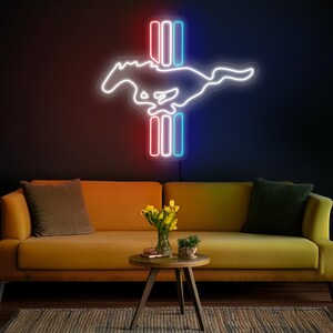 May include: A neon sign depicting the iconic Mustang horse and bar logo. The sign is illuminated in white, red, and blue neon lights. The sign is mounted on a dark wall above a yellow couch.
