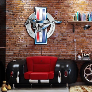 May include: A red leather couch shaped like a classic car with a chrome trim. The couch is in front of a brick wall with a Ford Mustang logo on it. The logo is silver and blue with the words "Ford" and "Mustang" on it.