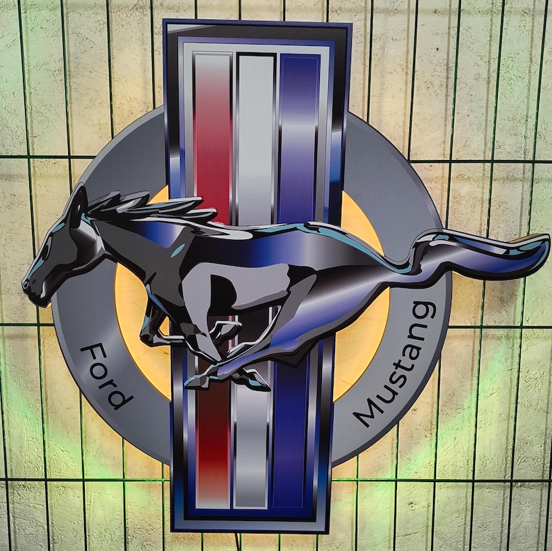 May include: A silver and blue Ford Mustang logo with a black running horse in the center. The logo has the words "Ford" and "Mustang" written on it.