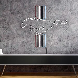 May include: A white neon sign of a running horse with a red, white, and blue vertical stripe design. The sign is mounted on a gray concrete wall above a black entertainment console.