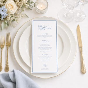 May include: A formal table setting with a menu card, plates, and silverware. The menu card has a blue border and elegant script. Gold-colored forks and a knife are placed on the white plates. A lit candle and flowers add to the ambiance.