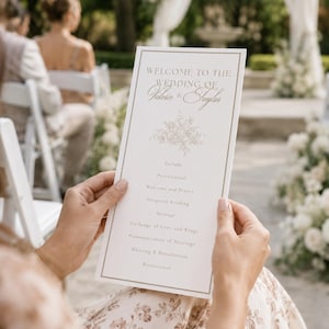 May include: A rectangular white wedding program card with a thin gold border, featuring the text "WELCOME TO THE WEDDING OF Valesie & Taylor" in gold, followed by a floral illustration and a list of ceremony events including Prelude and Recessional.